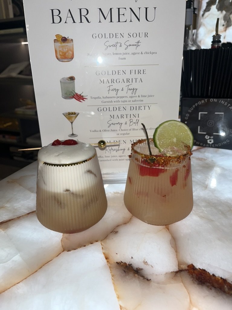 A custom Golden bar menu behind a Golden Sour and a Golden Fire Margarita on an onyx bar