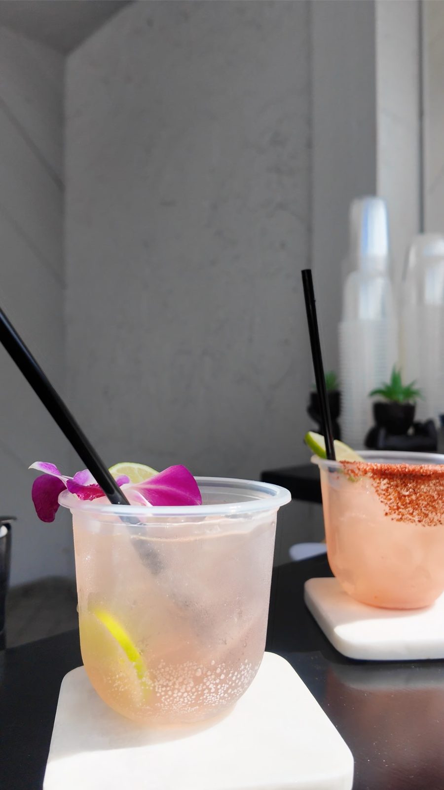 Two cocktails with orchid and lime garnish and a Tajín rim on marble coasters